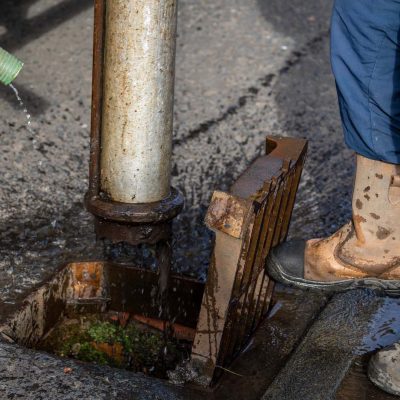 Gully sewer drain jet cleaning: Municipal Medium Volume Combination (MVC) Tanker Truck operative uses vacuum suction pipe in Suburban Street